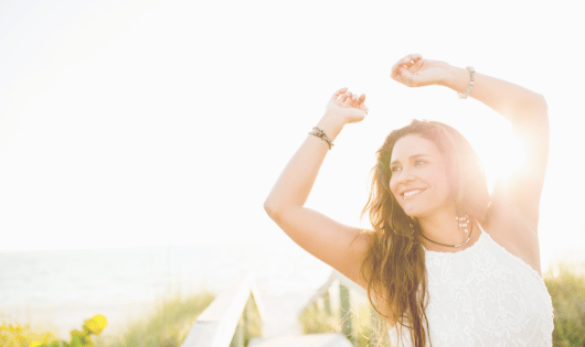 Woman in the sun with arms raised and smiling