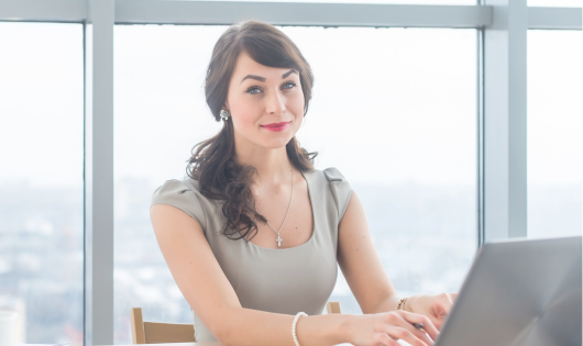 Woman sitting at desk looking straight at camera with a mona lisa smile